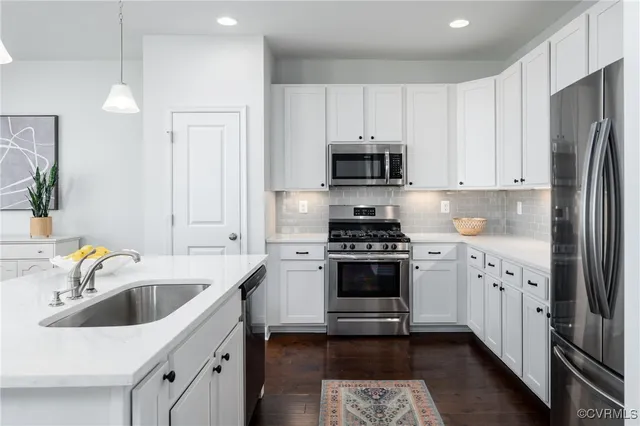 a kitchen with stainless steel appliances a sink a stove a microwave a refrigerator a stove and white cabinets