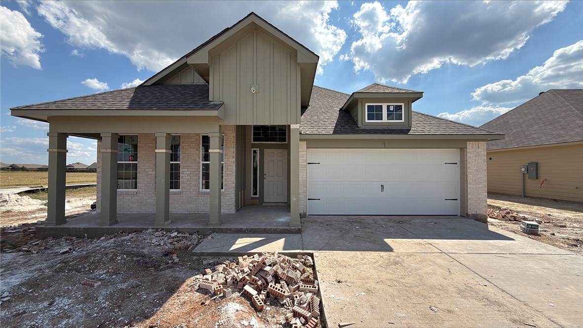 View of front of house with brick siding, a shingled roof, driveway, covered porch, and board and batten siding