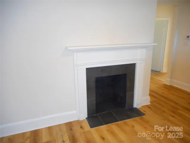 a view of an empty room with wooden floor and a fireplace