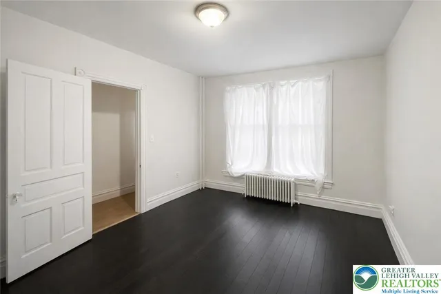 an empty room with wooden floor and windows with curtains