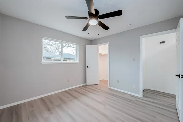an empty room with wooden floor ceiling fan and windows