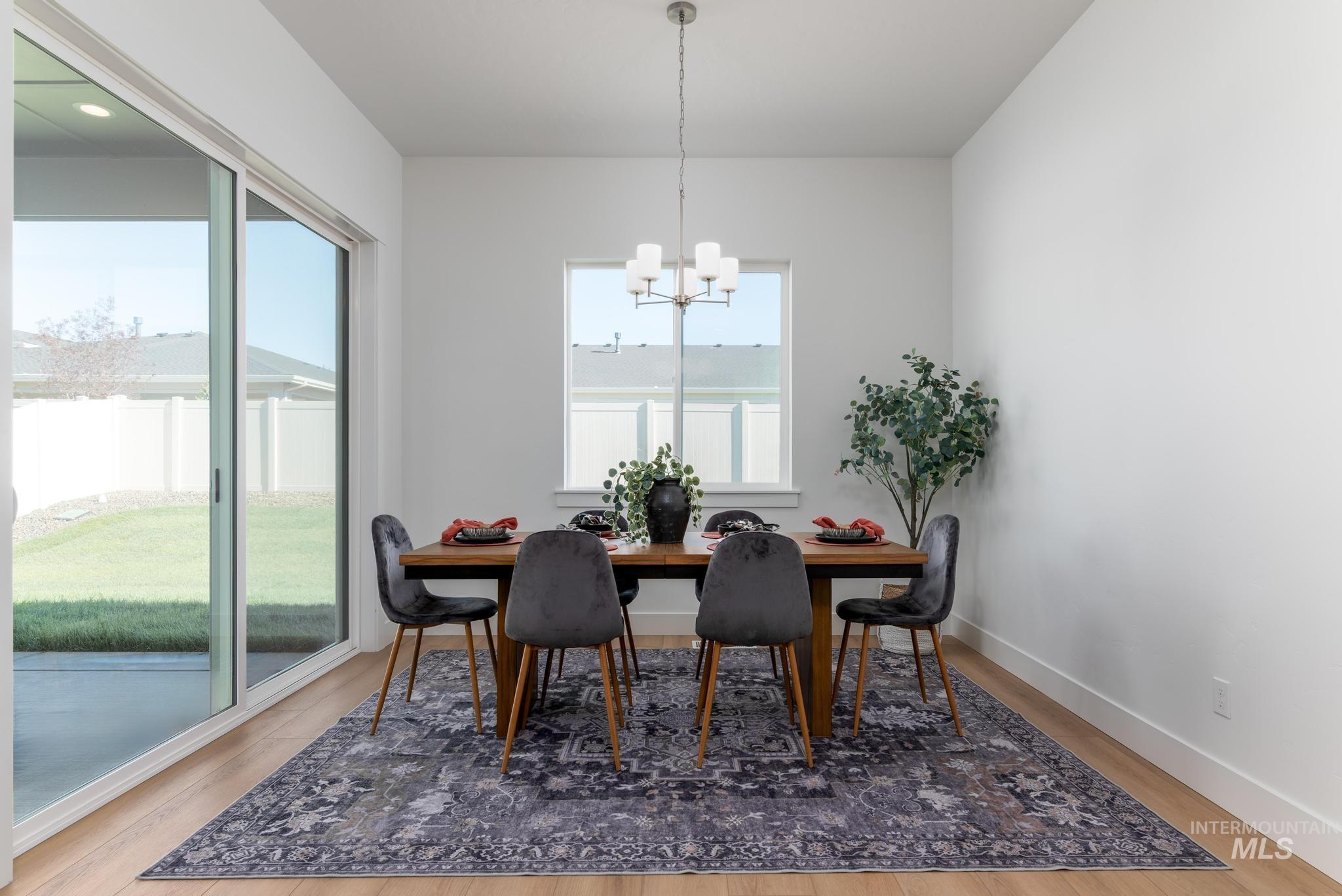 9074 West Moonglade Street Star, ID 83669 - Photo 18 of 40 Dining space featuring wood-finish flooring, a contemporary chandelier, a large picture window, and a sliding glass door opening to an outdoor patio