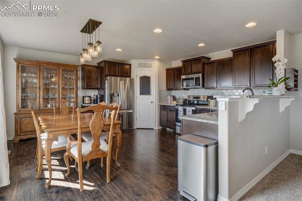 11305 Avena Road Peyton, CO 80831 - Photo 8 of 47 a kitchen with stainless steel appliances kitchen island granite countertop a dining table chairs refrigerator and microwave