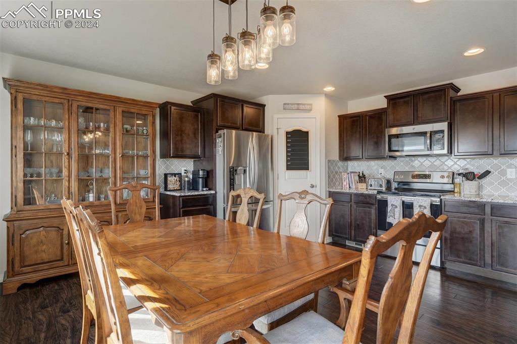 11305 Avena Road Peyton, CO 80831 - Photo 9 of 47 a dining room with stainless steel appliances granite countertop a stove a refrigerator a kitchen island a dining table and chairs