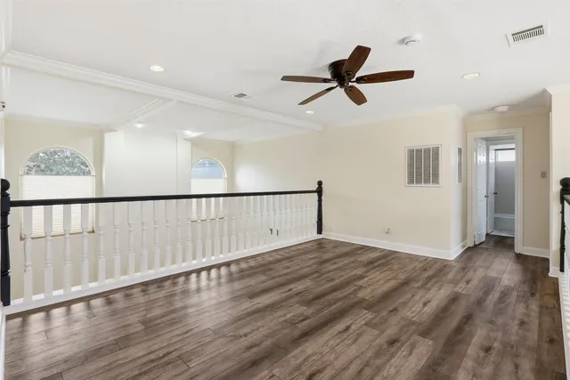 an empty room with wooden floor chandelier fan and windows