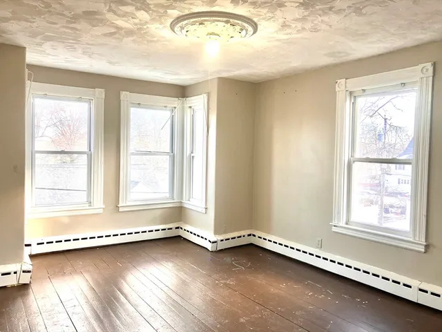 a view of an empty room with a window and wooden floor