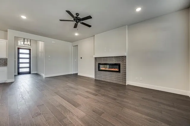 an empty room with wooden floor a ceiling fan a fireplace and windows
