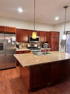 a kitchen with stainless steel appliances granite countertop a sink a stove a refrigerator a center island with wooden floor and cabinets