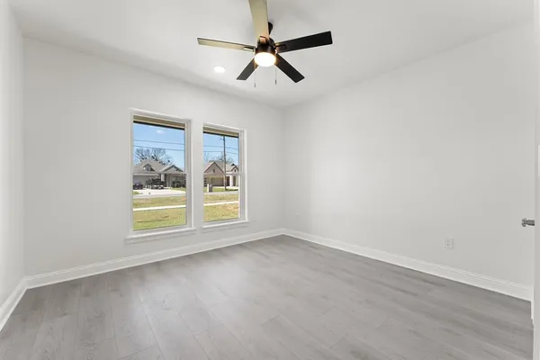 an empty room with wooden floor ceiling fan and windows