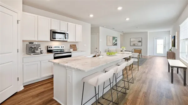 a kitchen with stainless steel appliances kitchen island granite countertop a stove a sink a refrigerator and white cabinets with wooden floor