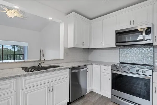 a kitchen with granite countertop white cabinets appliances a sink and a window