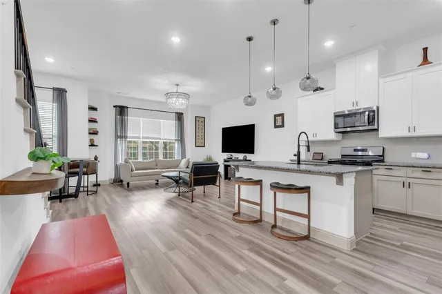 a living room with stainless steel appliances kitchen island granite countertop a stove a sink a dining table and chairs with wooden floor