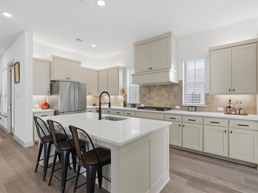 9533 Keep Street Frisco, TX 75035 - Photo 8 of 40 Kitchen featuring an expansive center island with seating, light-toned cabinetry, stainless steel appliances, and wood-finish flooring