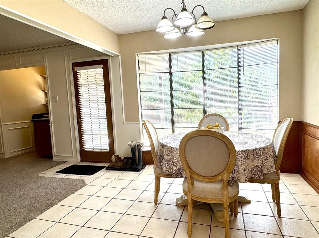 113 Northeast Timber Ridge Drive Burleson, TX 76028 - Photo 12 of 36 Dining area featuring large bay windows, ceramic tile flooring, a multi-light chandelier, and wainscoting with wood paneling