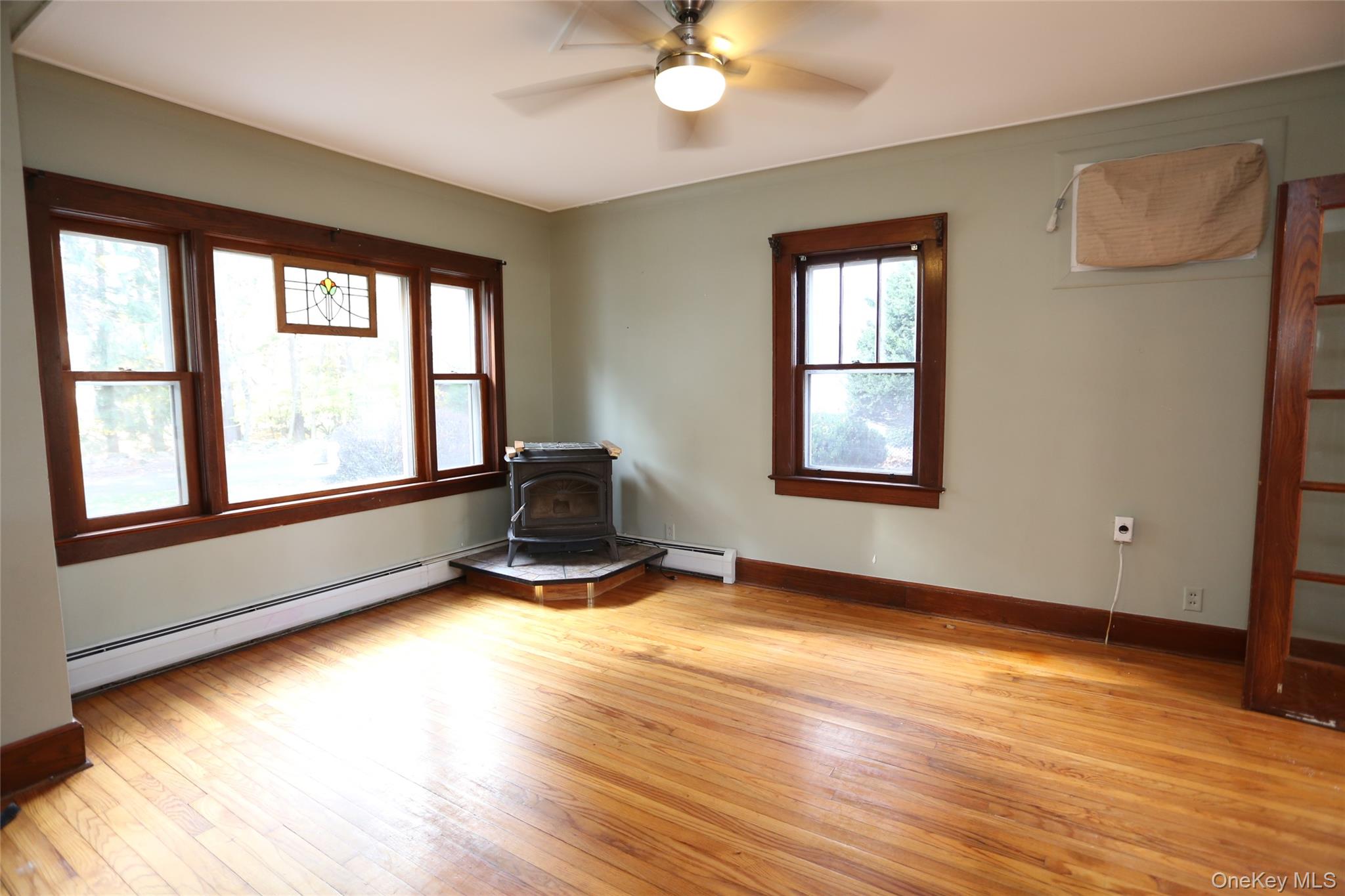 113 Brewery Road New City, NY 10956 - Photo 8 of 39 Unfurnished room featuring a baseboard heating unit, a wood stove, light wood-type flooring, and a ceiling fan