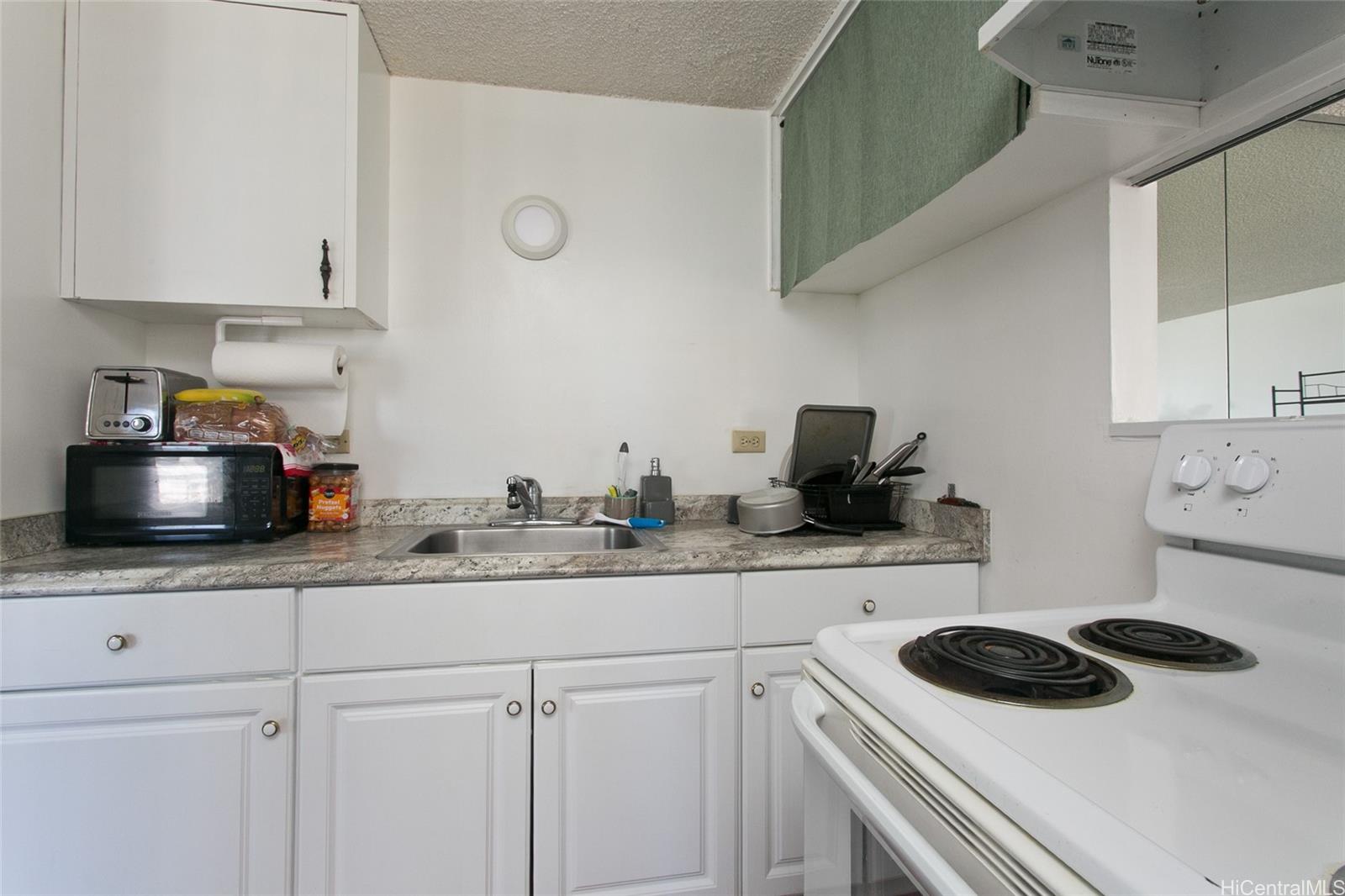 2525 Date Street, Unit 1705 Honolulu, HI 96826 - Photo 5 of 11 a kitchen with white cabinets and a stove with wooden floor