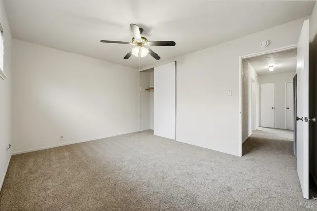 an empty room with chandelier fan and windows