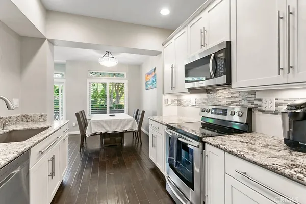 a kitchen with stainless steel appliances granite countertop a stove top oven a sink dishwasher and white cabinets with wooden floor