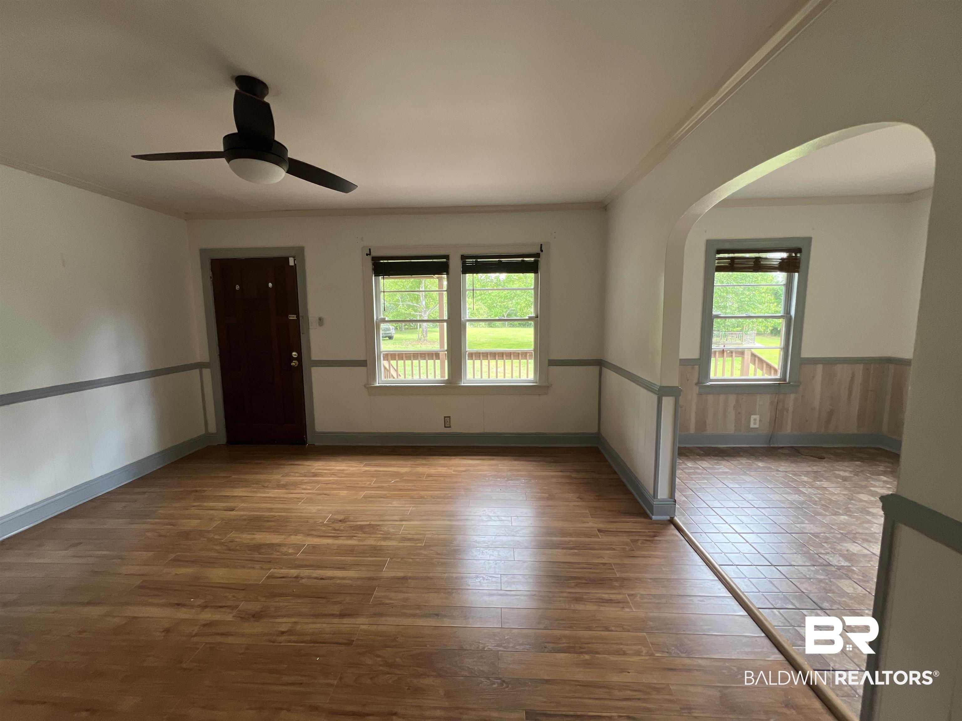 13301 A Hugh Fort Road Grand Bay, AL 36541 - Photo 6 of 34 Empty room with arched walkways, crown molding, a wainscoted wall, wood finished floors, and a ceiling fan