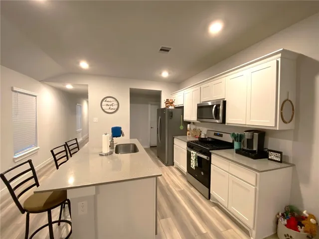 a kitchen with stainless steel appliances granite countertop a sink a stove a refrigerator with white cabinets and wooden floor