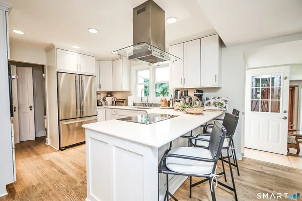 a kitchen with stainless steel appliances a refrigerator a stove a sink dishwasher a dining table and chairs with wooden floor