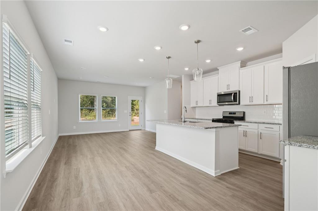 7830 Marie Way Fairburn, GA 30213 - Photo 6 of 30 a kitchen with stainless steel appliances kitchen island granite countertop a stove a sink a refrigerator and white cabinets with wooden floor