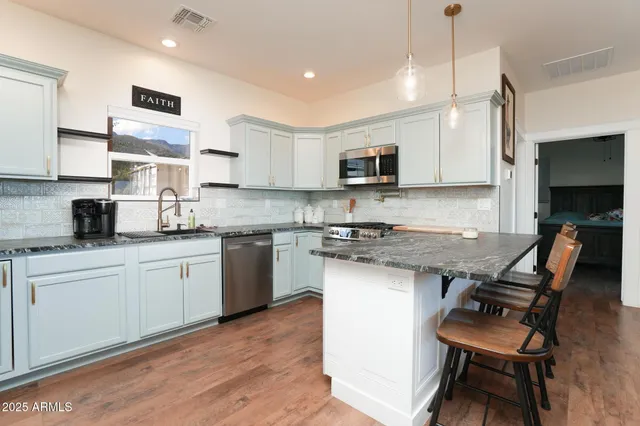a kitchen with stainless steel appliances kitchen island granite countertop a sink a stove and a wooden floors