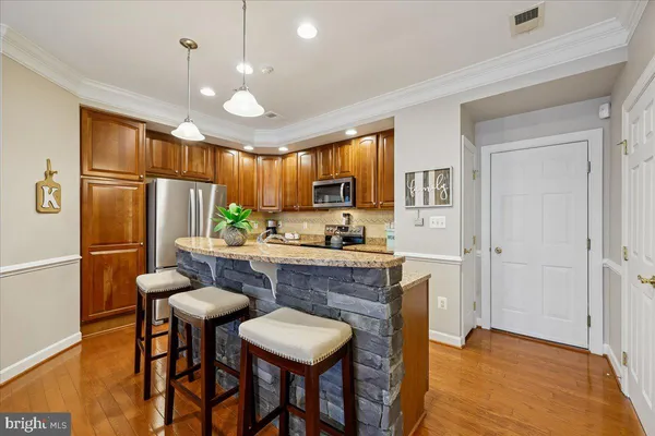 a kitchen with stainless steel appliances granite countertop a refrigerator a stove a sink a dining table and chairs with wooden floor