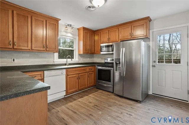 a kitchen with stainless steel appliances granite countertop a refrigerator a sink dishwasher a stove with wooden cabinets and floor