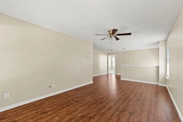 a view of an empty room with wooden floor and a ceiling fan