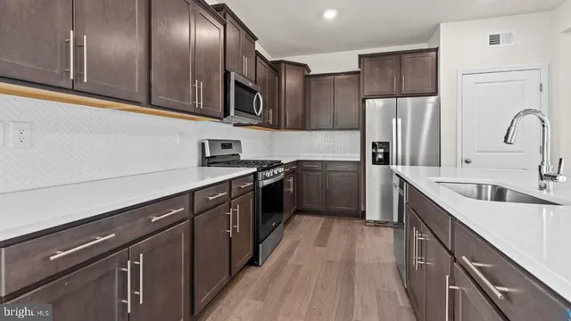 a kitchen with stainless steel appliances a sink dishwasher a refrigerator a stove top oven with wooden floor