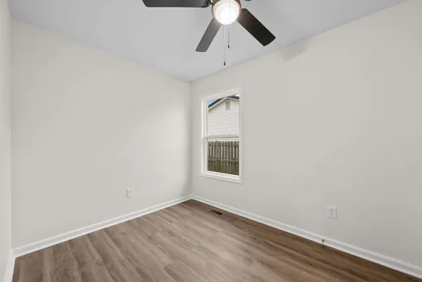 an empty room with wooden floor chandelier fan and windows