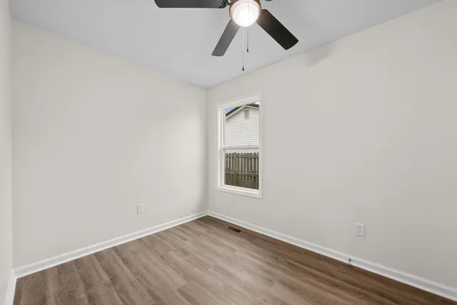 an empty room with wooden floor chandelier fan and windows