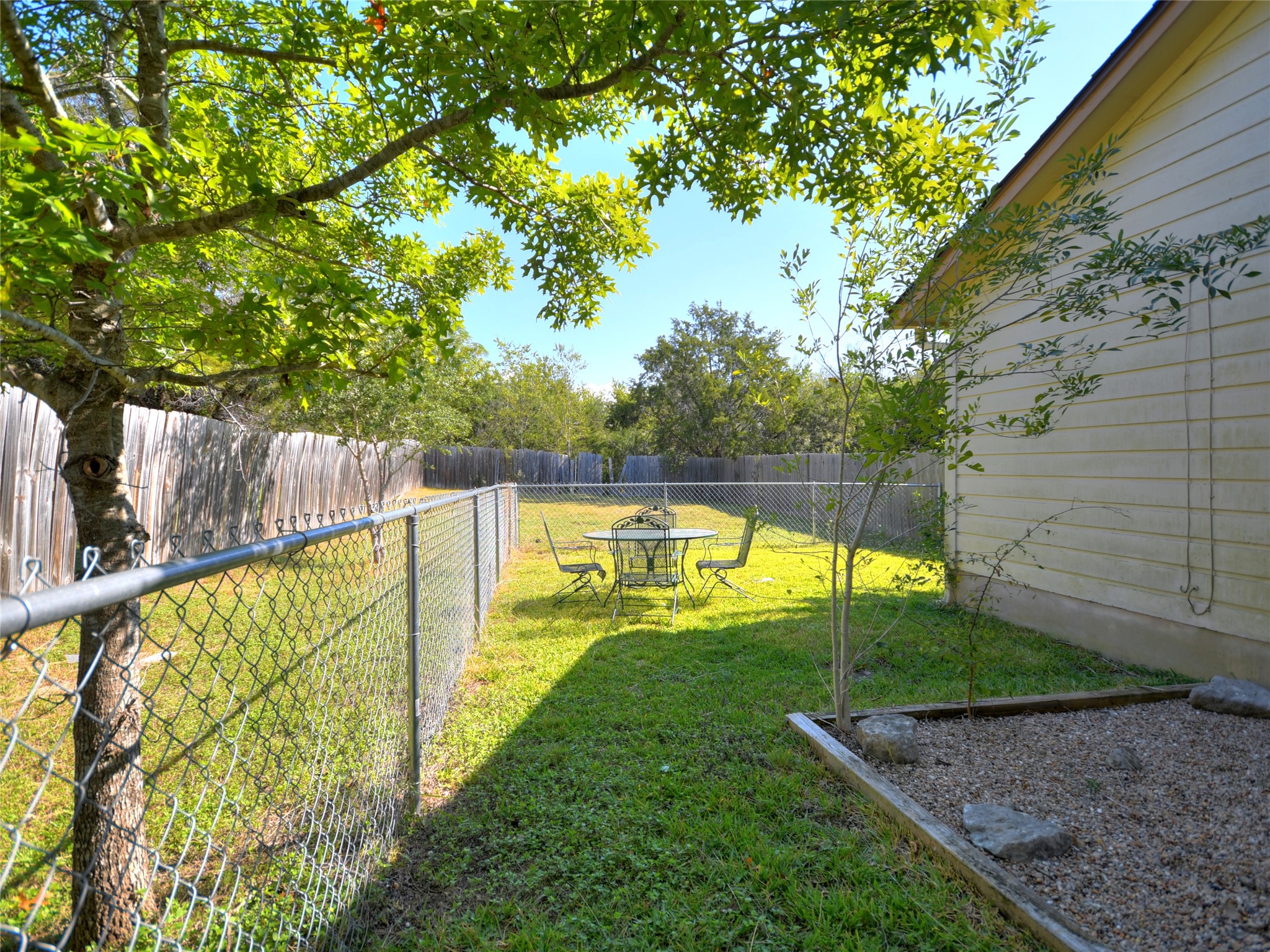 415 Fantail Loop, Unit A Austin, TX 78734 - Photo 14 of 15 Expansive grassy yard area with a chain-link fence, mature shade tree, and wood privacy fencing