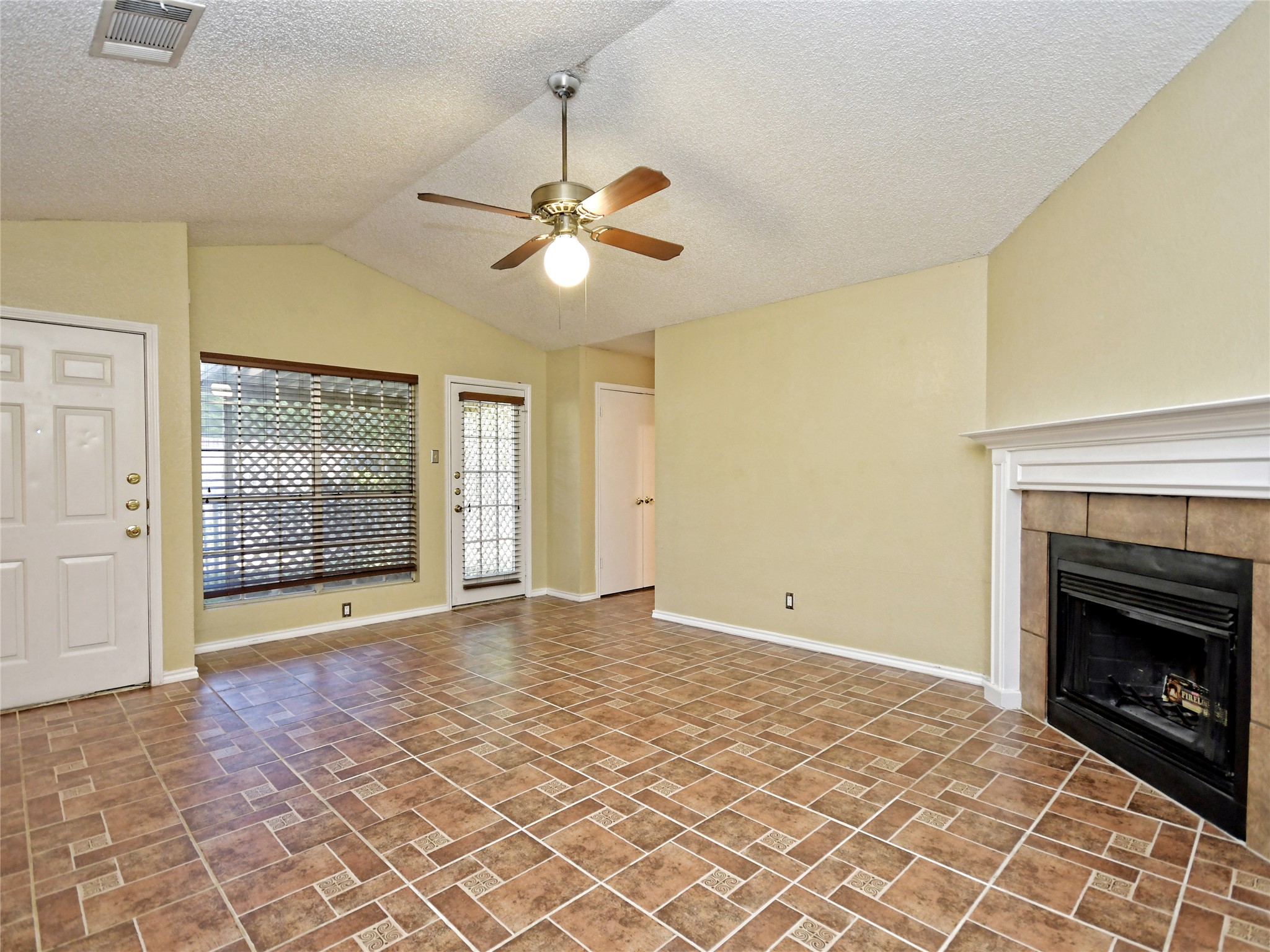 415 Fantail Loop, Unit A Austin, TX 78734 - Photo 3 of 15 Living area featuring a corner fireplace with a tile surround and white mantel, vaulted ceiling, and tile flooring
