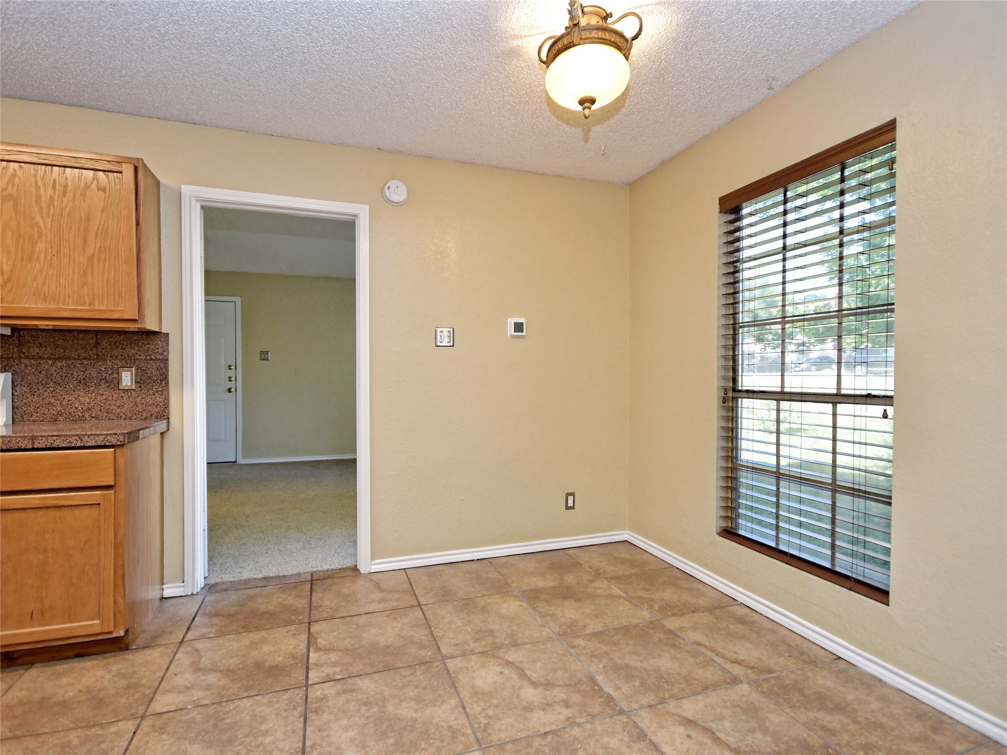 415 Fantail Loop, Unit A Austin, TX 78734 - Photo 5 of 15 Kitchen area featuring tile flooring, wooden cabinetry, a speckled countertop with a matching backsplash, and a window with blinds