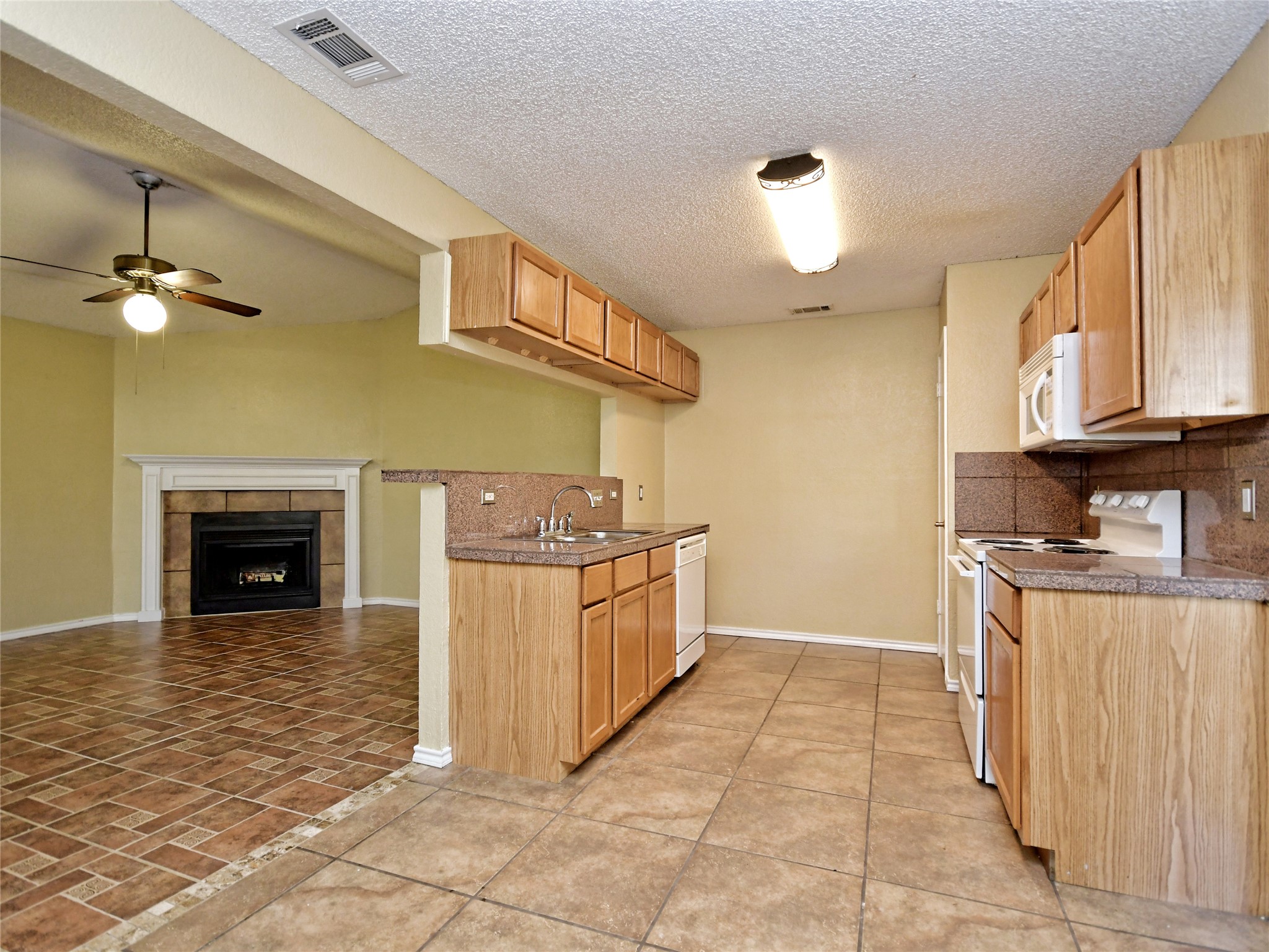 415 Fantail Loop, Unit A Austin, TX 78734 - Photo 6 of 15 Kitchen and living area featuring wood-finish cabinetry, a breakfast bar, stone-look countertops, and a tile backsplash