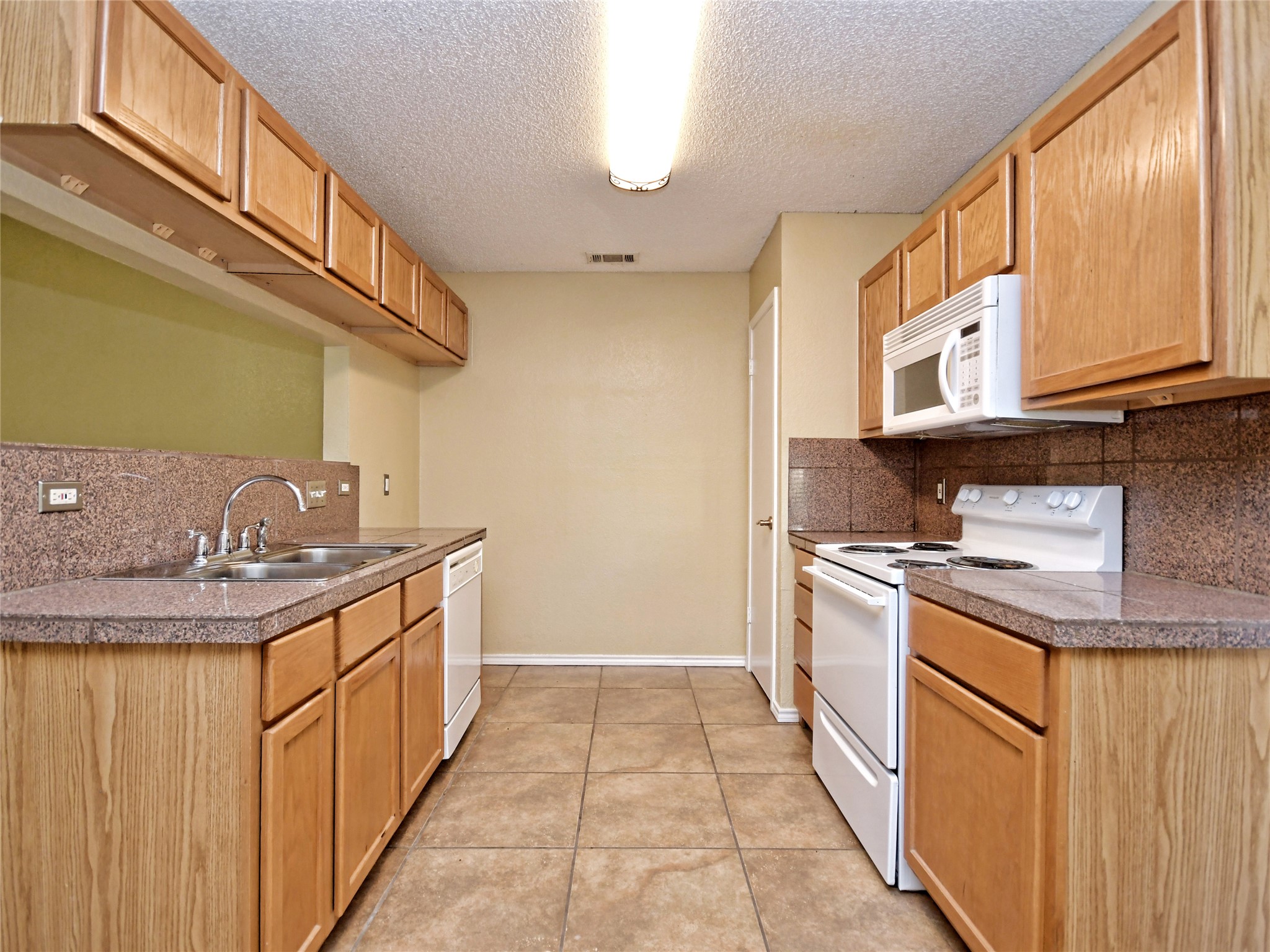 415 Fantail Loop, Unit A Austin, TX 78734 - Photo 7 of 15 Kitchen featuring wood-finish cabinetry, stone-look countertops, and a tile backsplash