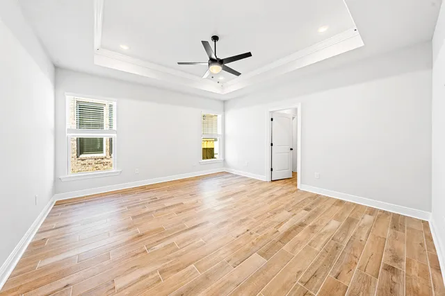 an empty room with wooden floor ceiling fan and windows