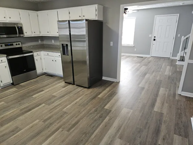 a kitchen with granite countertop a refrigerator stove and white cabinets with wooden floor