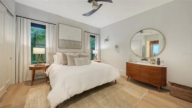 a bedroom with a bed a mirror on dresser and a large window