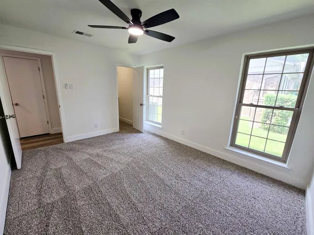 an empty room with chandelier fan and windows