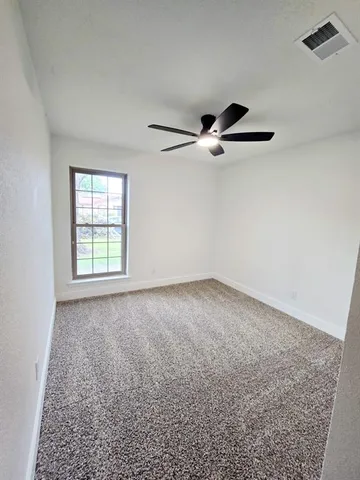 an empty room with ceiling fan and windows