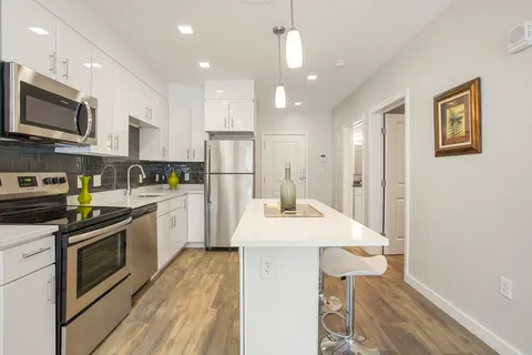 a kitchen with stainless steel appliances kitchen island granite countertop a refrigerator a stove top oven a sink dishwasher and white cabinets with wooden floor