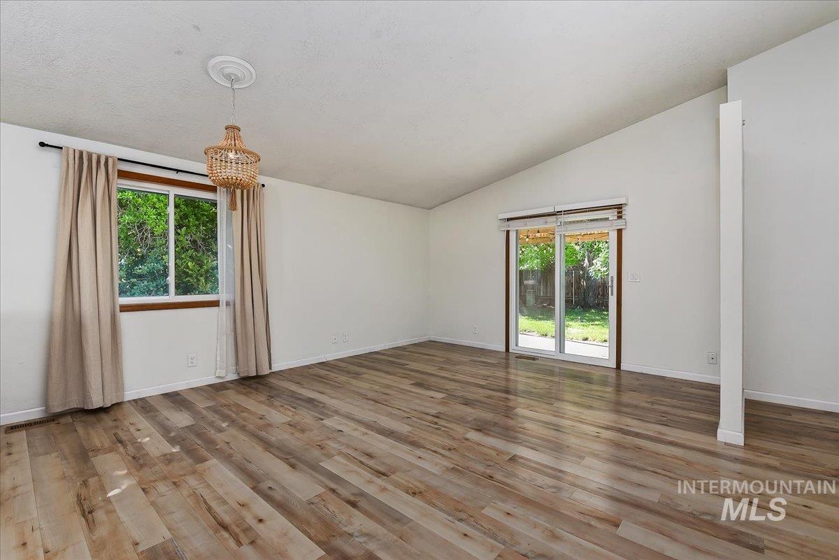 9215 West Preece Street Boise, ID 83704 - Photo 4 of 22 Vaulted ceiling room featuring wood-finish flooring, a contemporary woven chandelier, a large window, and a glass sliding door providing access to the backyard