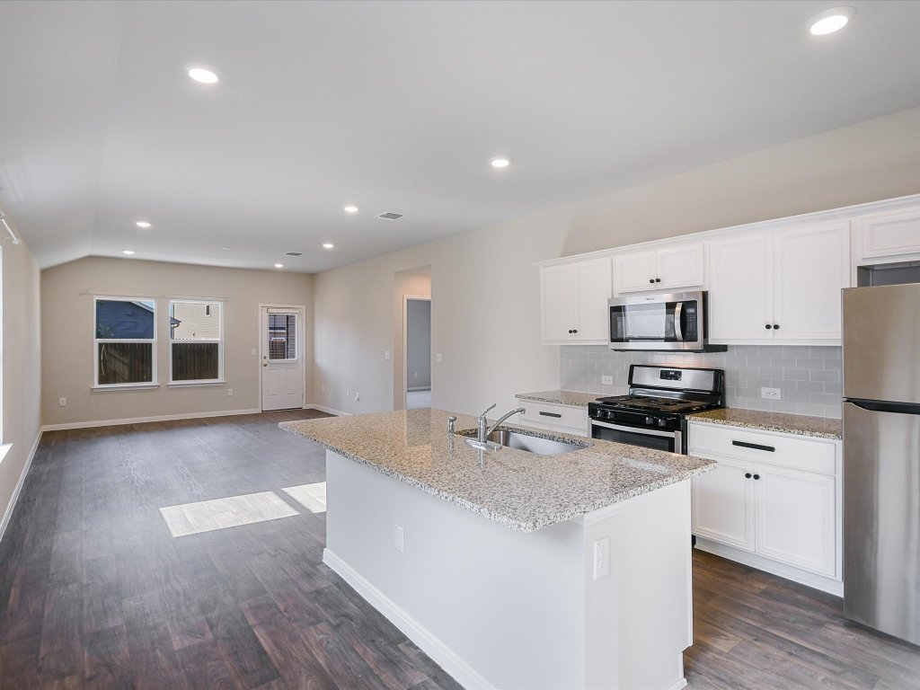 14408 Boquist Drive Pflugerville, TX 78660 - Photo 4 of 20 a large kitchen with stainless steel appliances granite countertop a stove a sink a refrigerator and white cabinets with wooden floor