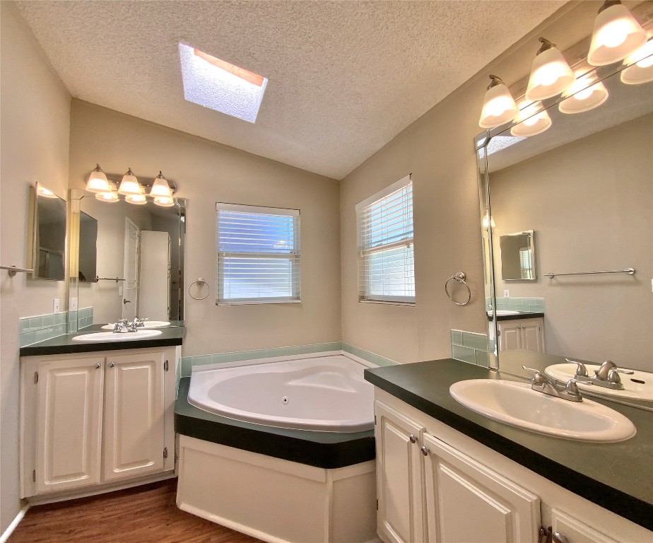 1301 Lipan Trail Austin, TX 78733 - Photo 14 of 39 Bathroom featuring two vanities, a textured ceiling, a skylight, a tub with jets, and lofted ceiling