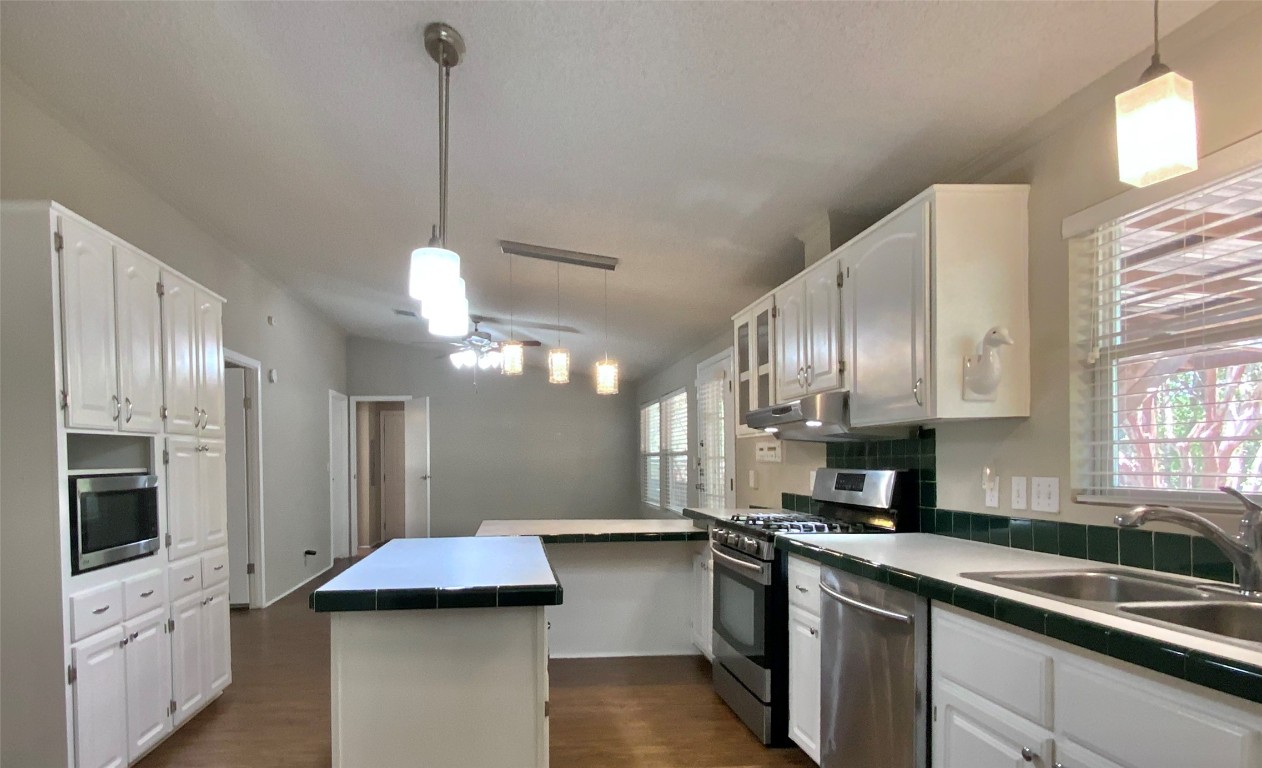 1301 Lipan Trail Austin, TX 78733 - Photo 23 of 39 Kitchen with hanging light fixtures, appliances with stainless steel finishes, dark wood finished floors, and tile countertops