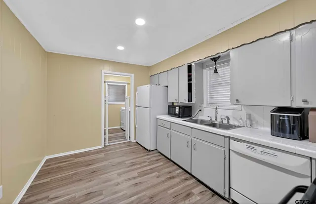 a kitchen with granite countertop a refrigerator oven a sink dishwasher and white cabinets with wooden floor