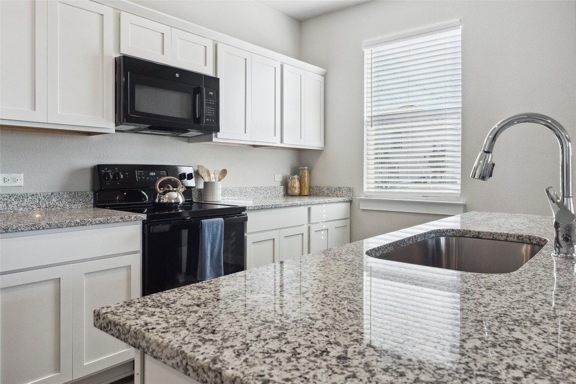 523 Powell Drive, Unit 1101 Leander, TX 78641 - Photo 11 of 24 Kitchen featuring black appliances, white cabinetry, and light stone counters